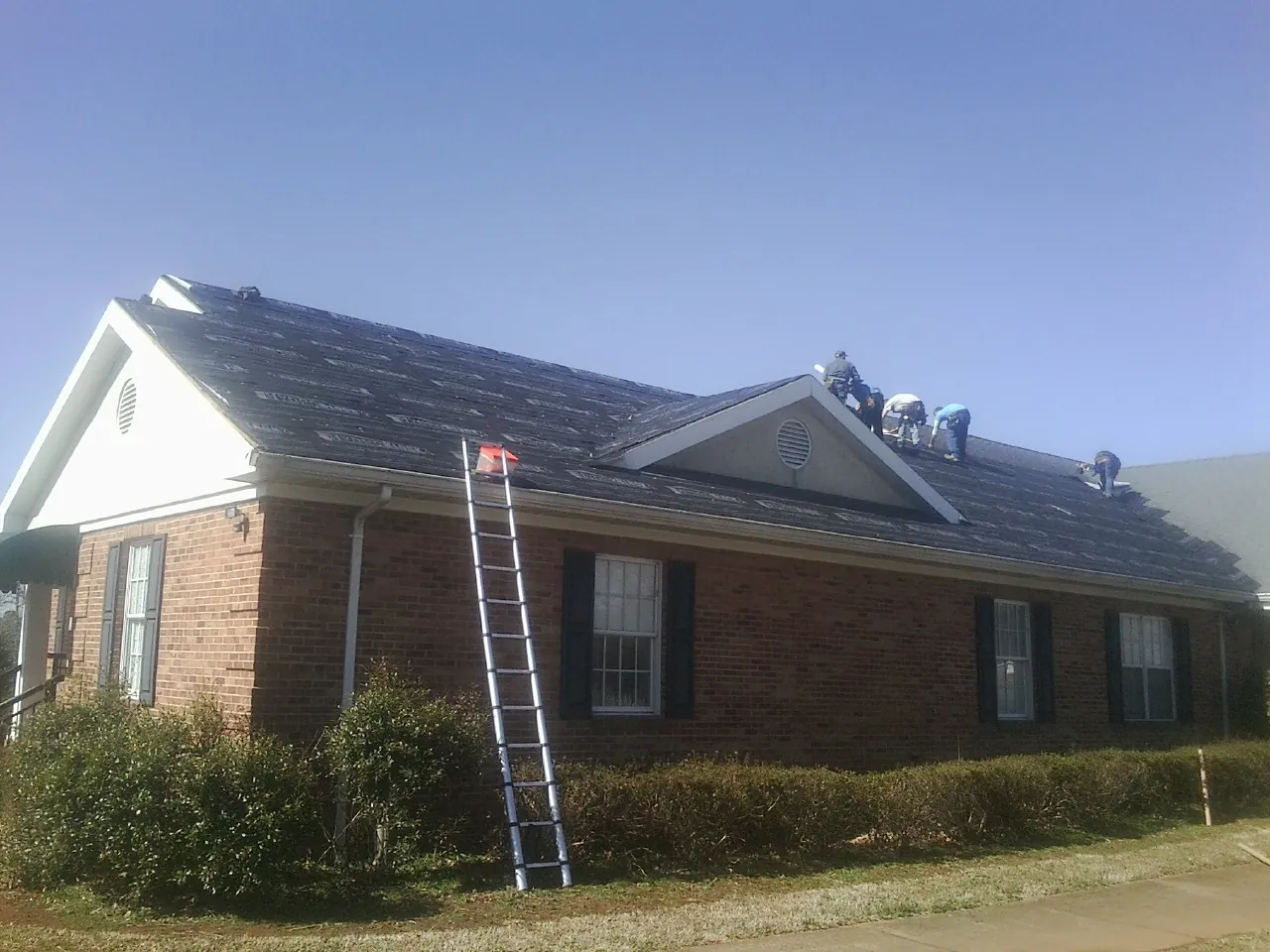 Crew tearing shingles off a brick ranch roof with a ladder set — Metal Roof Repair work by our crew in Myrtle Creek