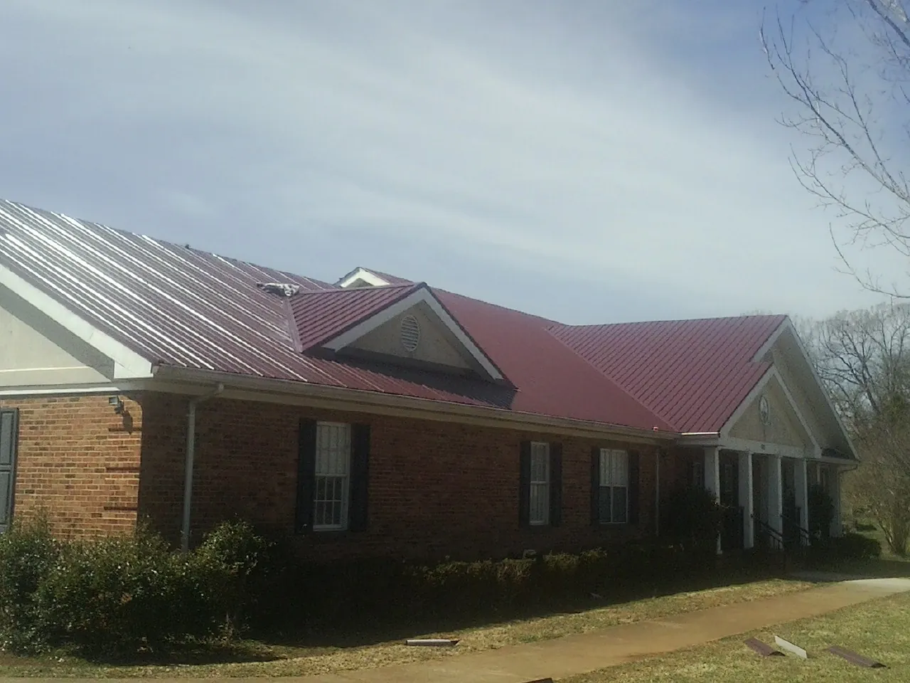Red metal roof with gabled entries on a long brick building, from a Hail Damage Roof Repair job in Myrtle Creek