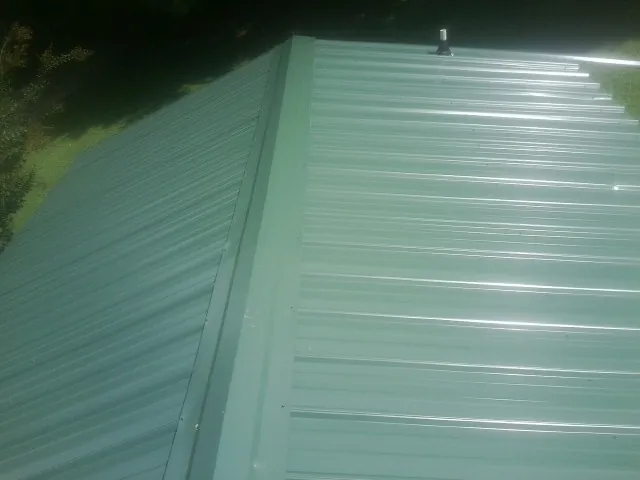 New green metal panels meeting at the ridge of a roof — Flat Roof Repair work by our crew in Myrtle Creek
