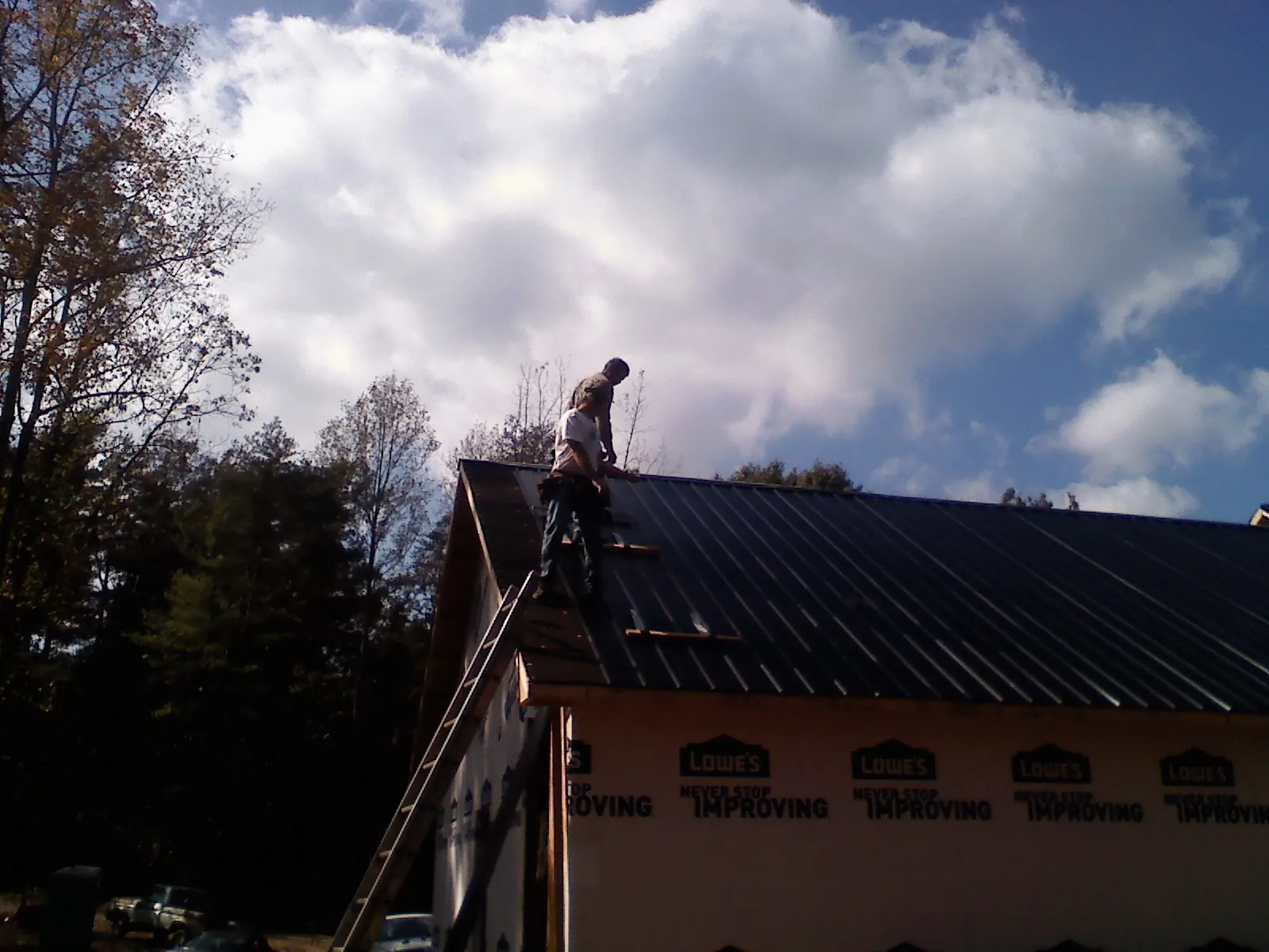 Roofer fastening dark metal panels high against a cloudy sky, from a Roof Inspection job in Myrtle Creek