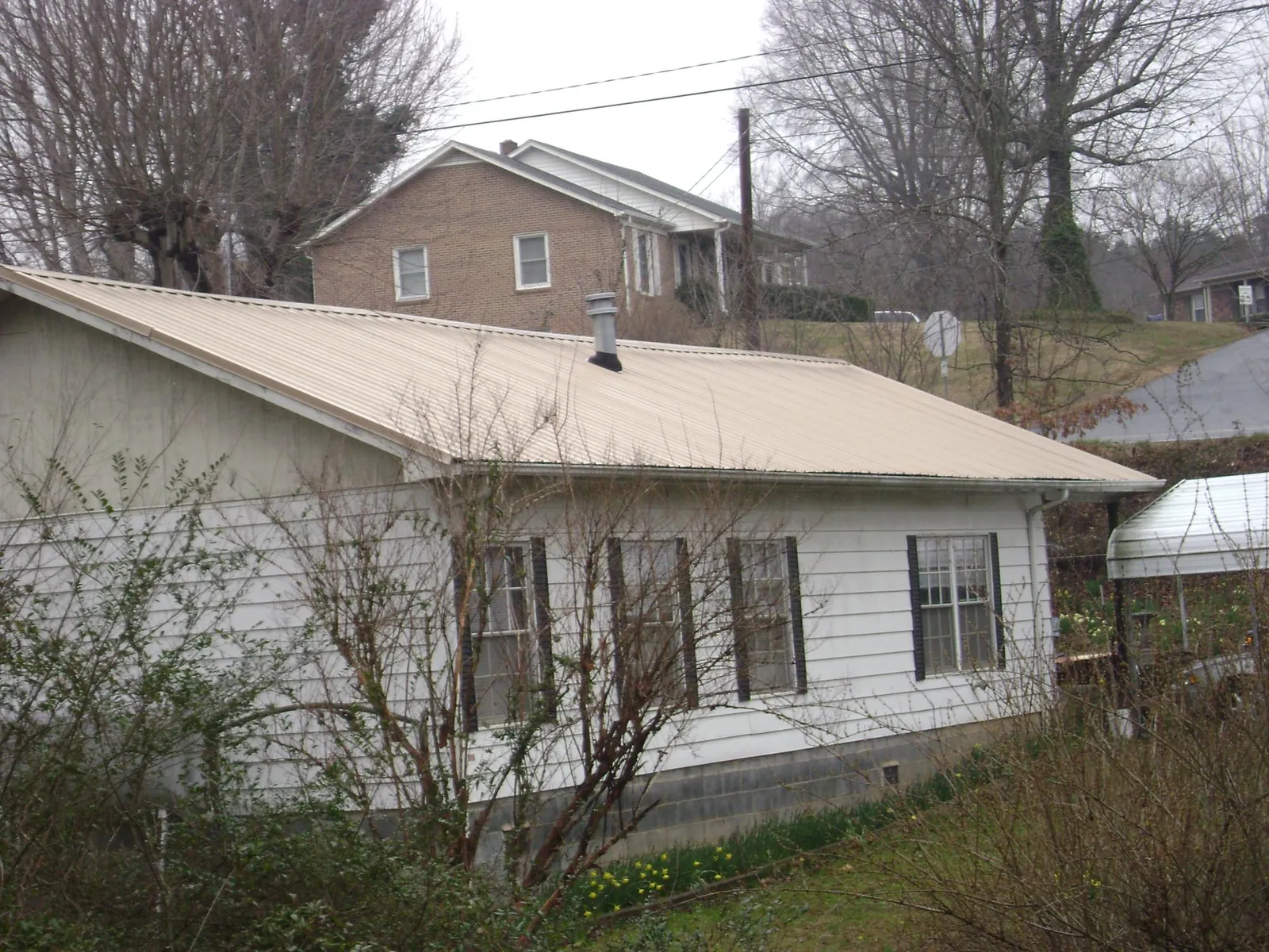 Tan metal roof on a white sided house set into a hillside — Commercial Roofing by Roofing Brothers in Myrtle Creek