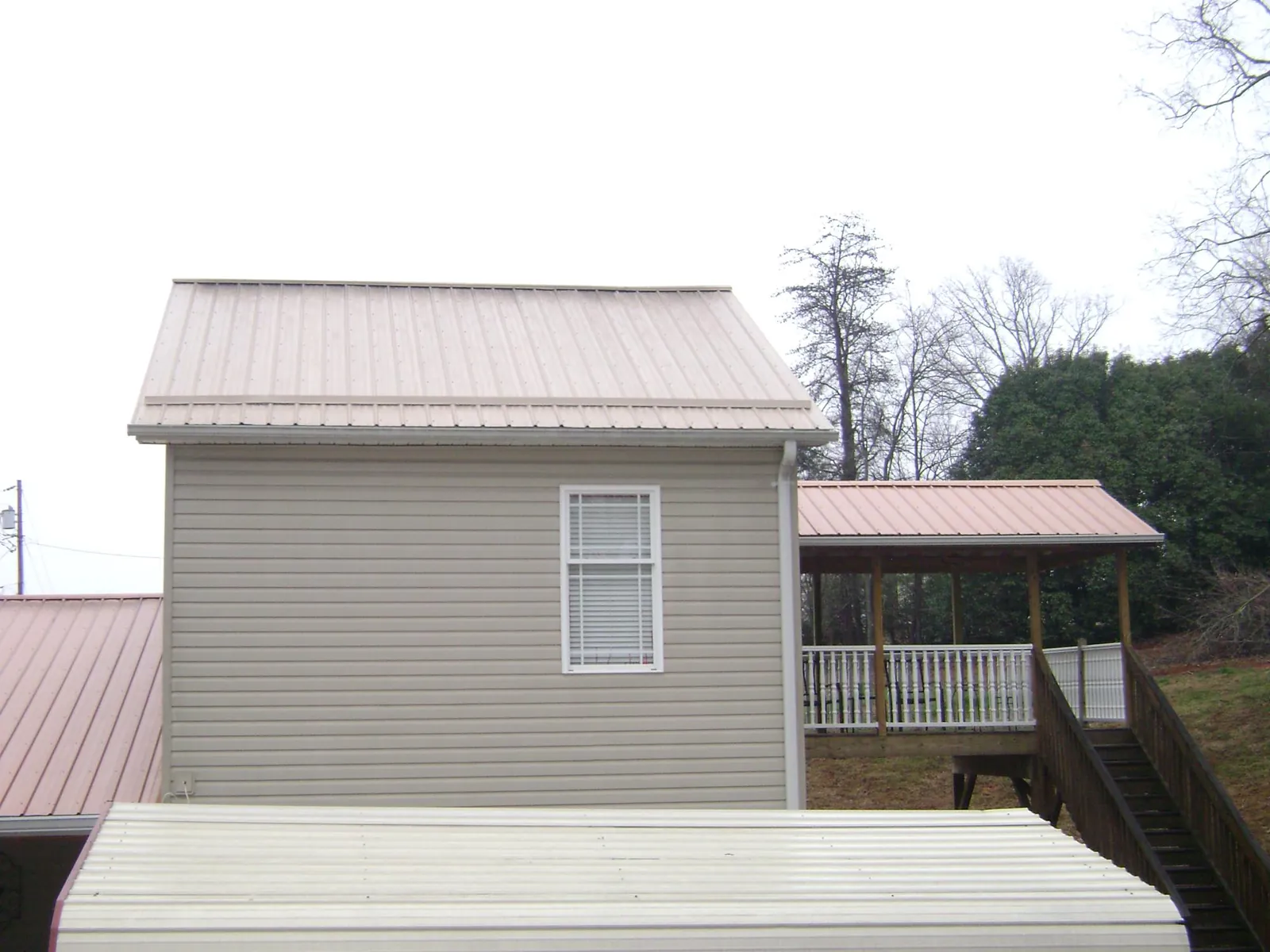 Tan metal roofs on a two story addition and attached porch, from a Roof Replacement job in Myrtle Creek